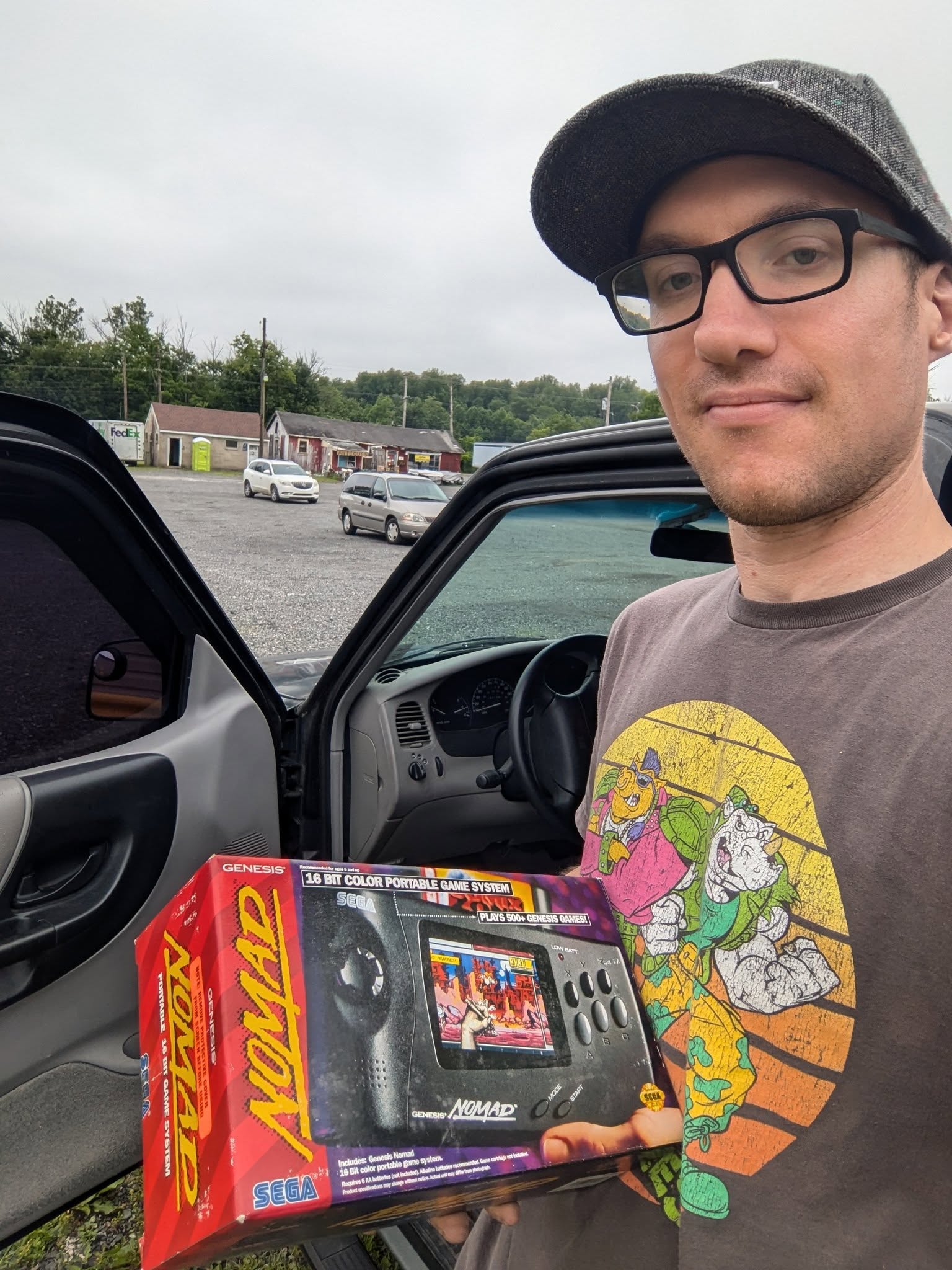 Greg holding a boxed Sega Nomad beside his vehicle