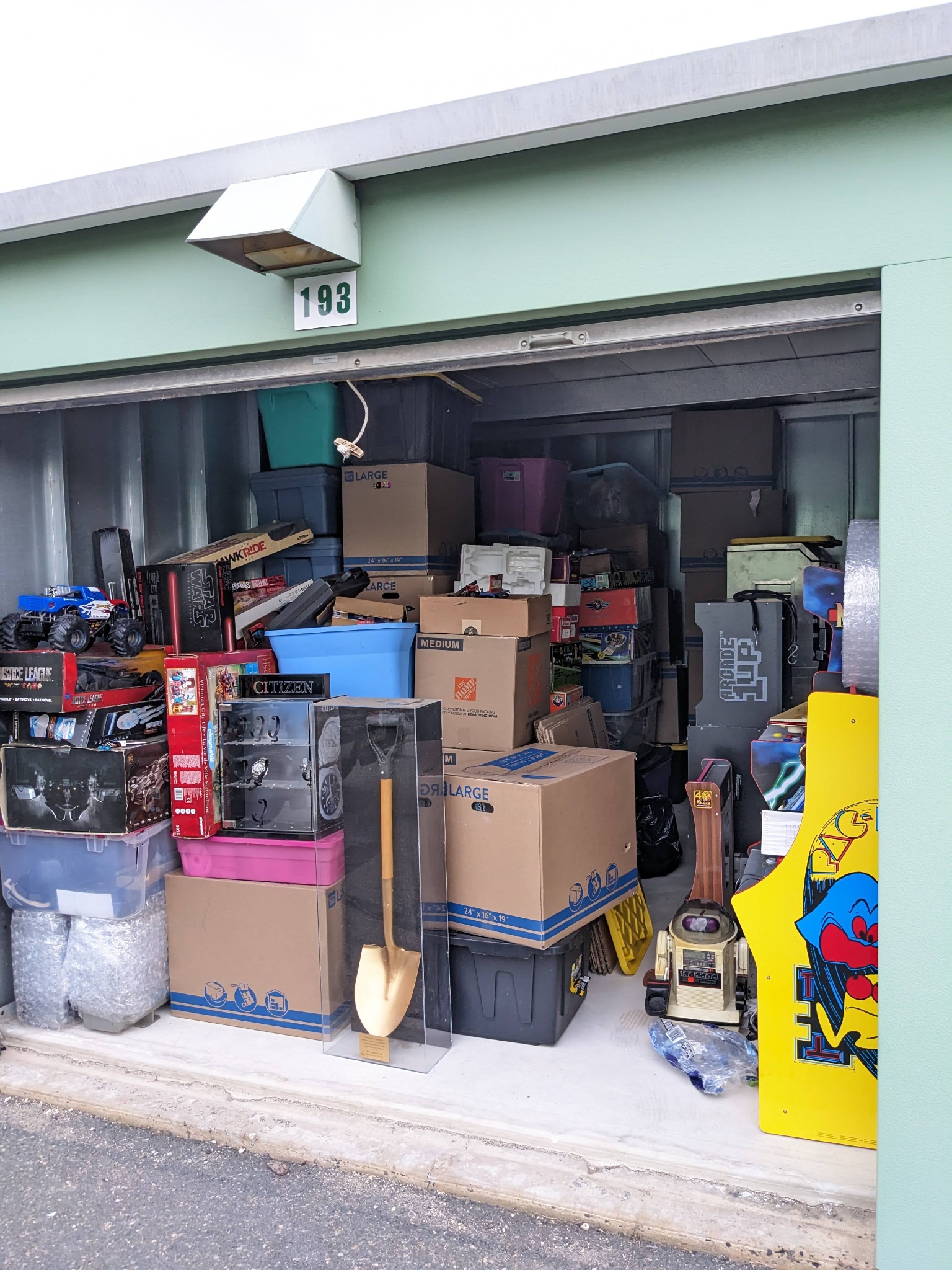 A storage unit containing a varied real collection, including boxes, display material, hobby objects, and an arcade cabinet side